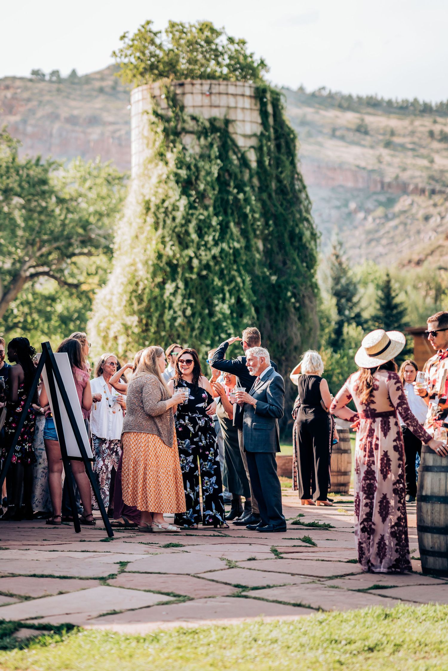 Outdoor wedding ceremony gathering with guests in front of ivy-covered stone structure.