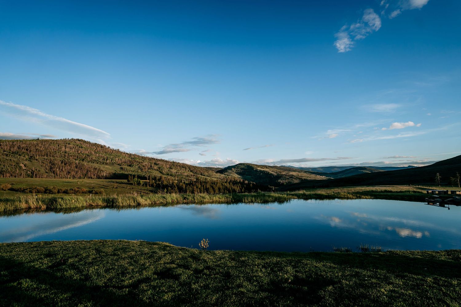 Serene mountain lake reflects blue sky and rolling hills in stunning landscape view.