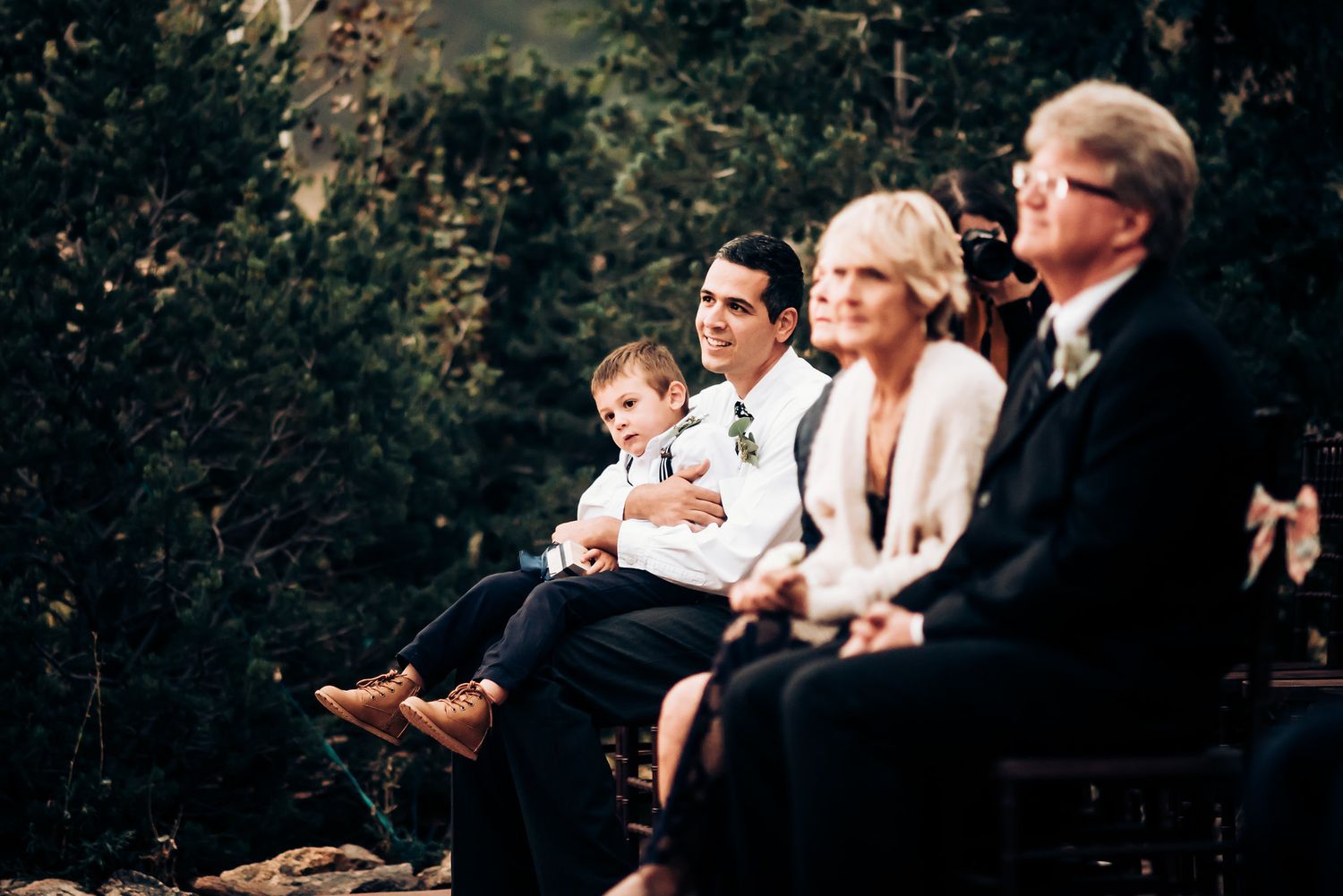 Wedding guests seated in formal attire watching the ceremony outdoors.