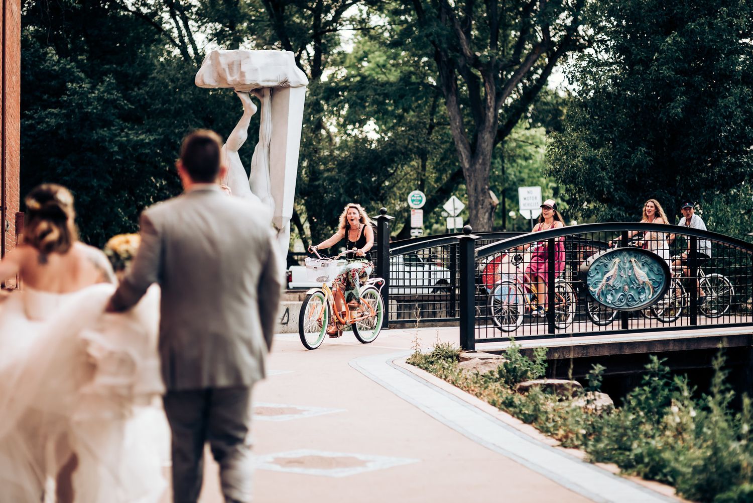 Wedding celebration interrupted by passing cyclists crossing bridge in background.