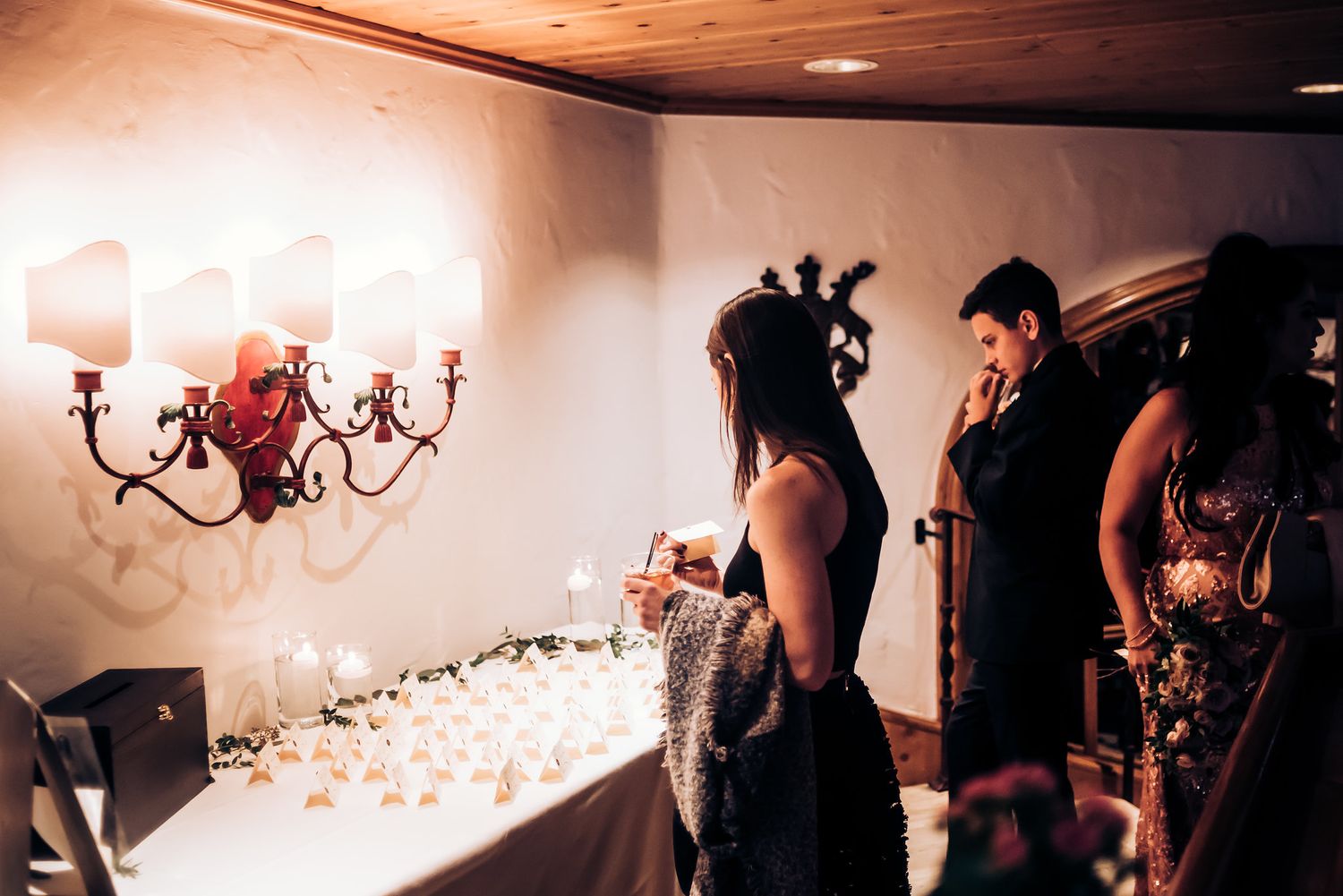 Guests gather in an elegantly lit reception space with wall sconces.