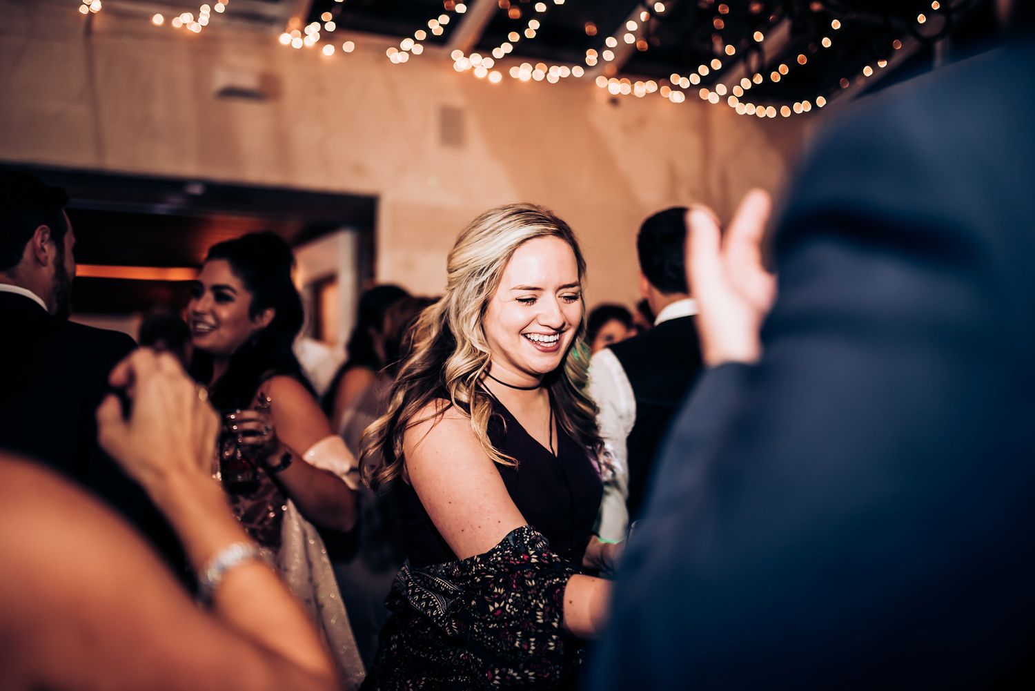 A guest in a sparkly black dress dances joyfully at an indoor celebration.