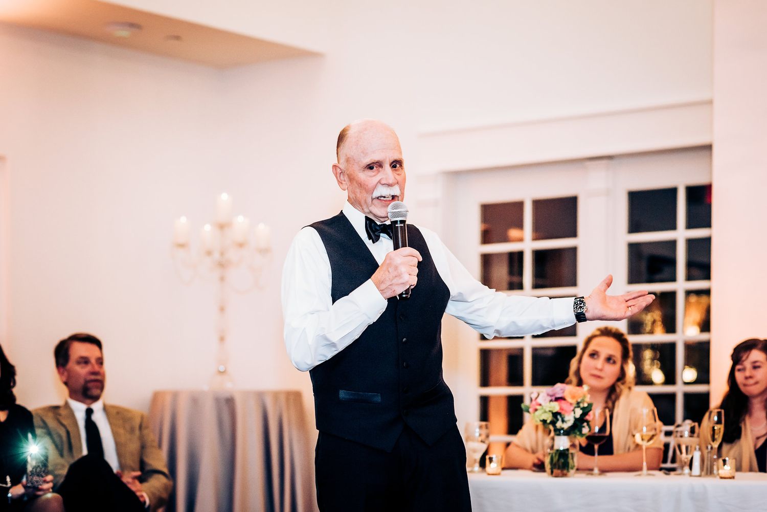 Speaker in formal attire giving emotional wedding speech during reception dinner.