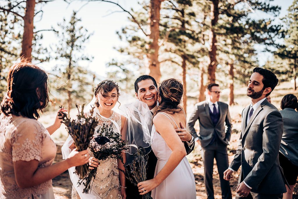 Wedding party shares joyful moments together in a sun-dappled forest setting.