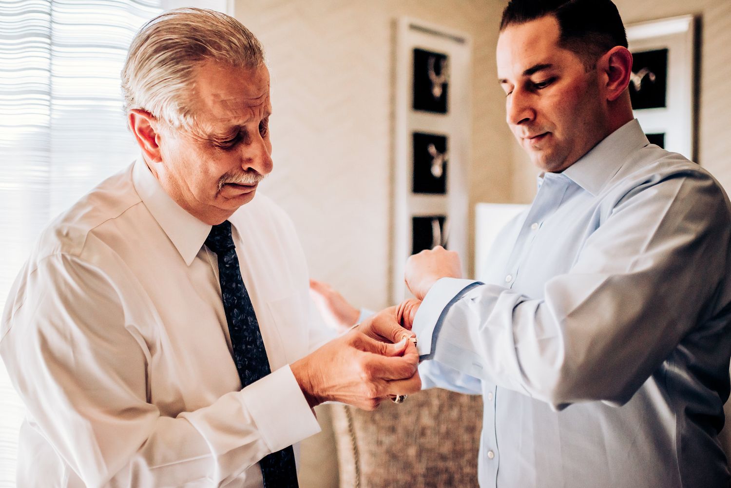 Two people in formal attire examine cufflinks during wedding preparations.