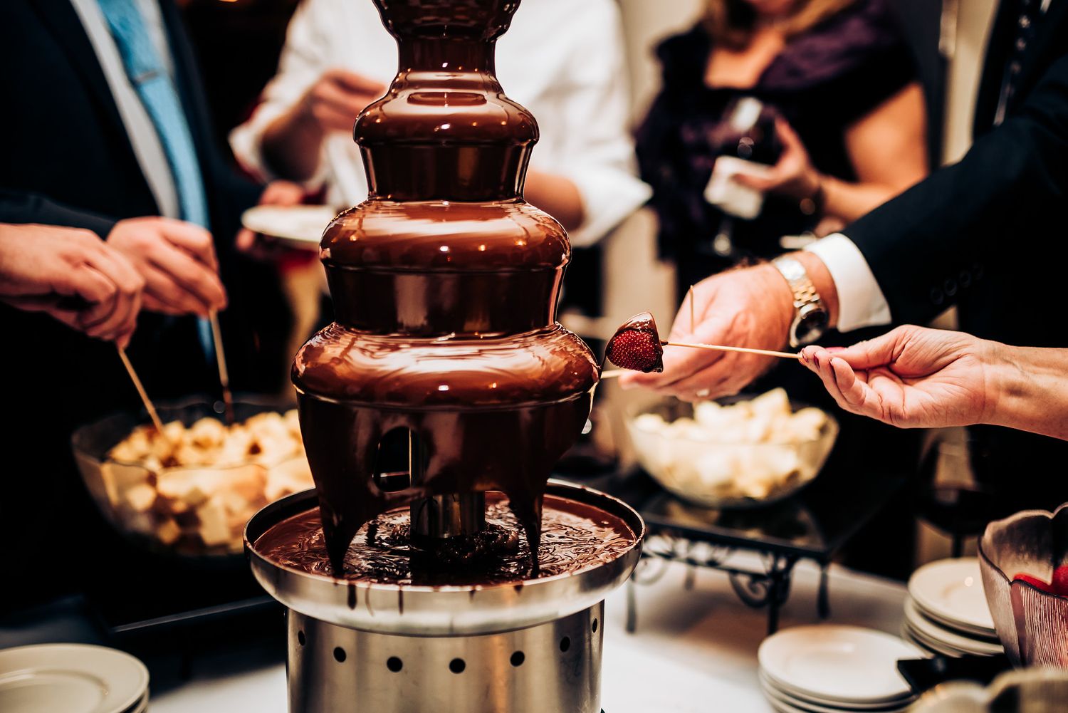 Guests gather around a chocolate fountain dessert station at a party.