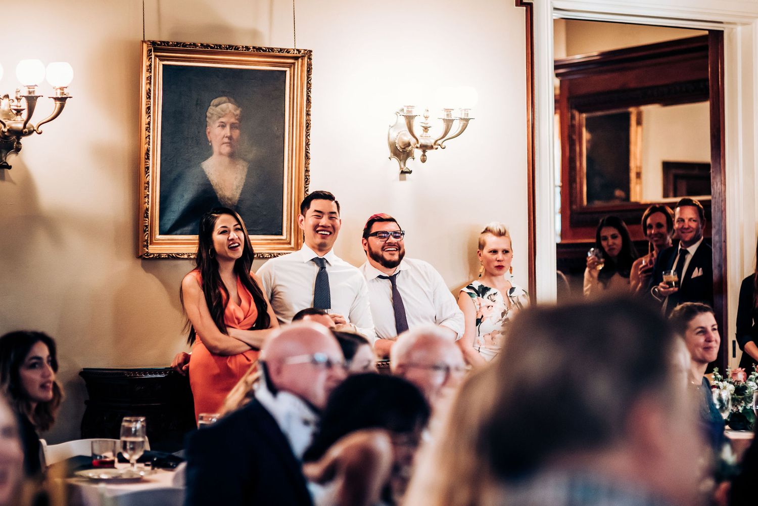 Reception guests gathered in an elegant dining room with classical portraits and wall sconces.
