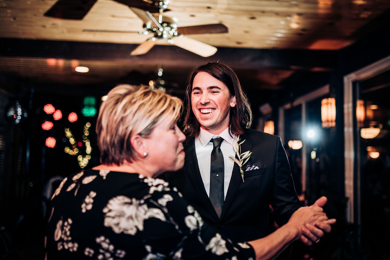 A joyous dance moment captured at an indoor reception venue with wooden ceiling and festive lighting.