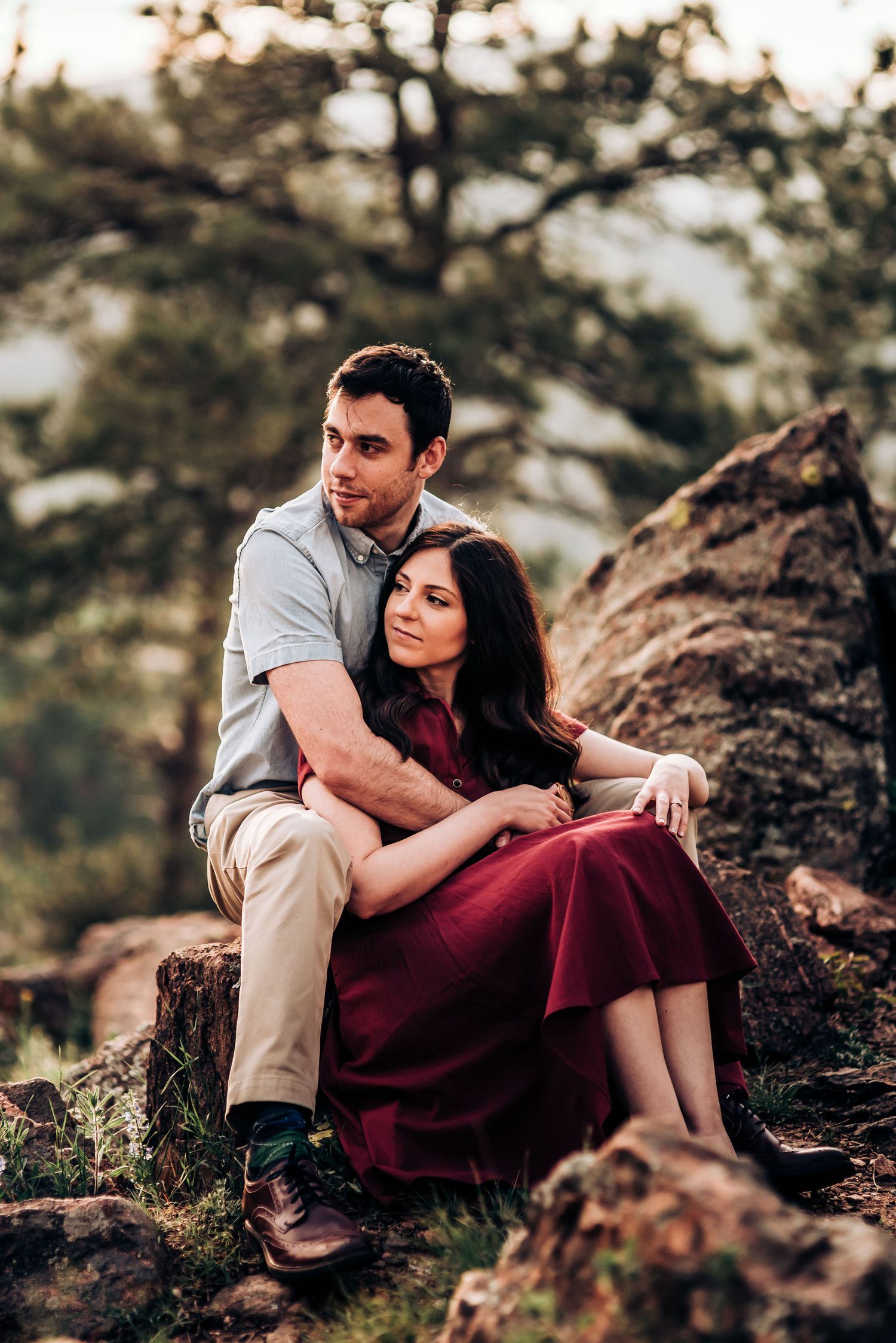 Couple embraces while sitting on rocky outcrop in mountain wilderness during golden hour sunset.