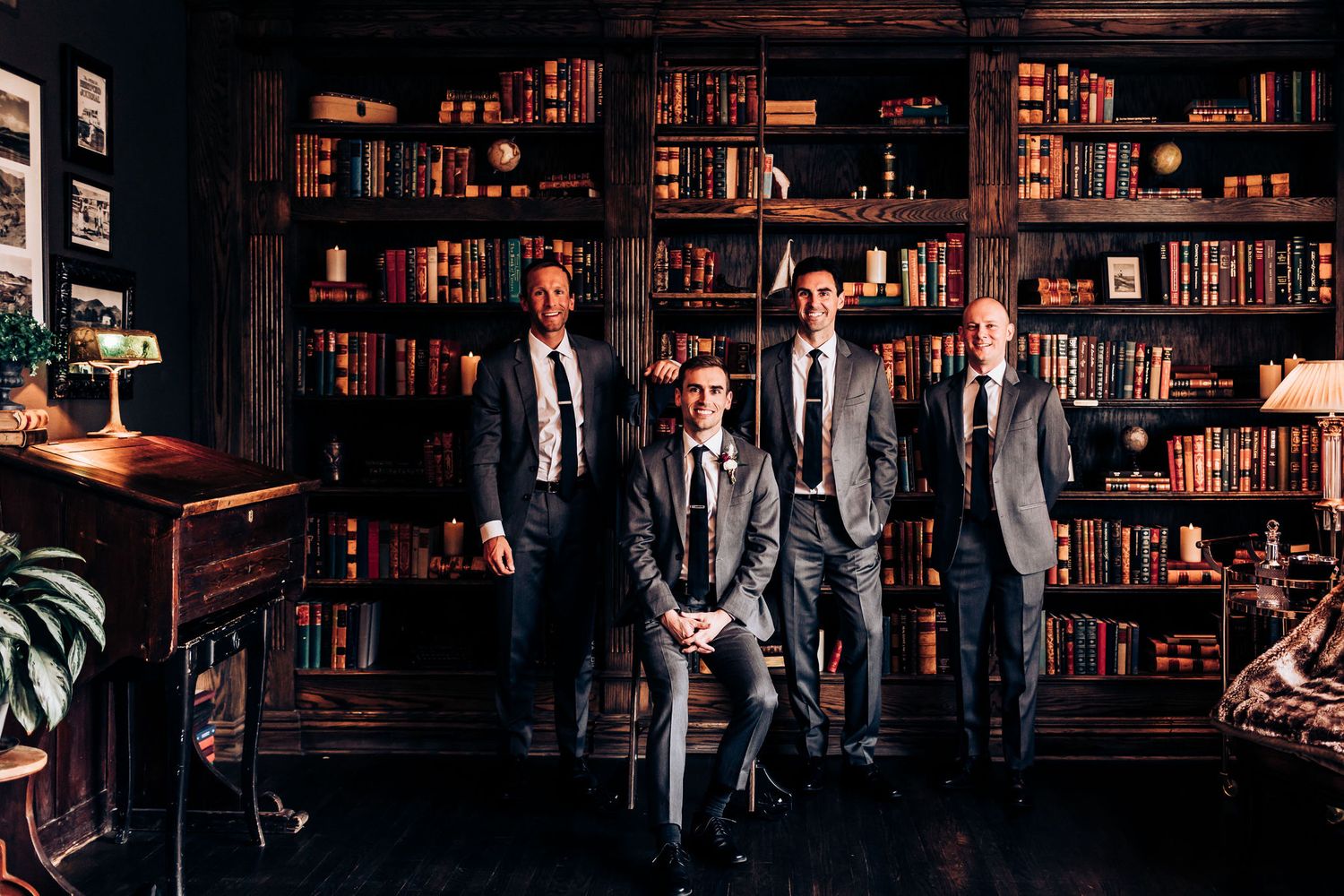 Group posing in formal attire against classic library backdrop with wooden shelves.