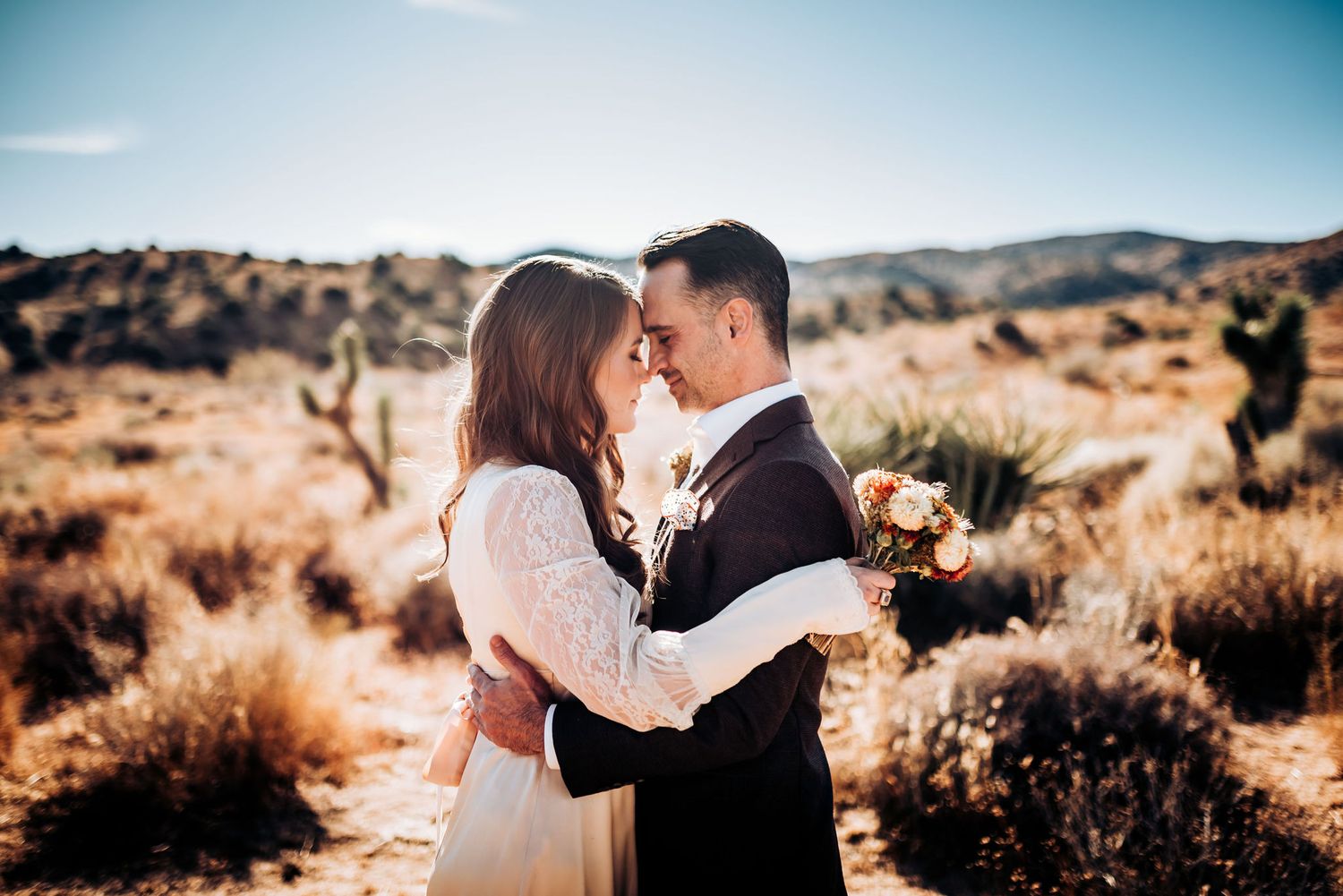 Romantic wedding moment captured in desert setting with mountains and golden light.