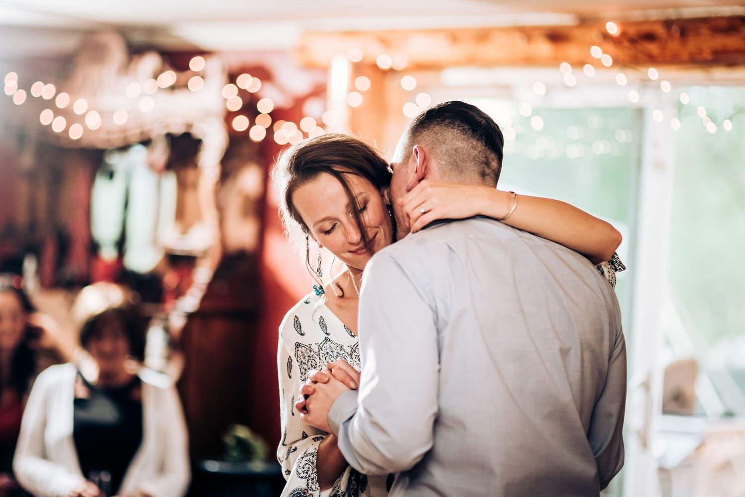 A tender moment between dancers illuminated by warm string lights at an indoor venue.