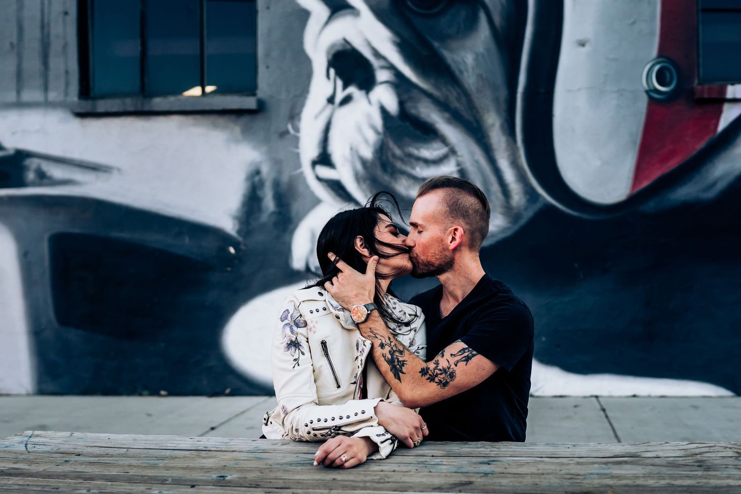 Couple shares romantic moment while sitting against large street art mural.