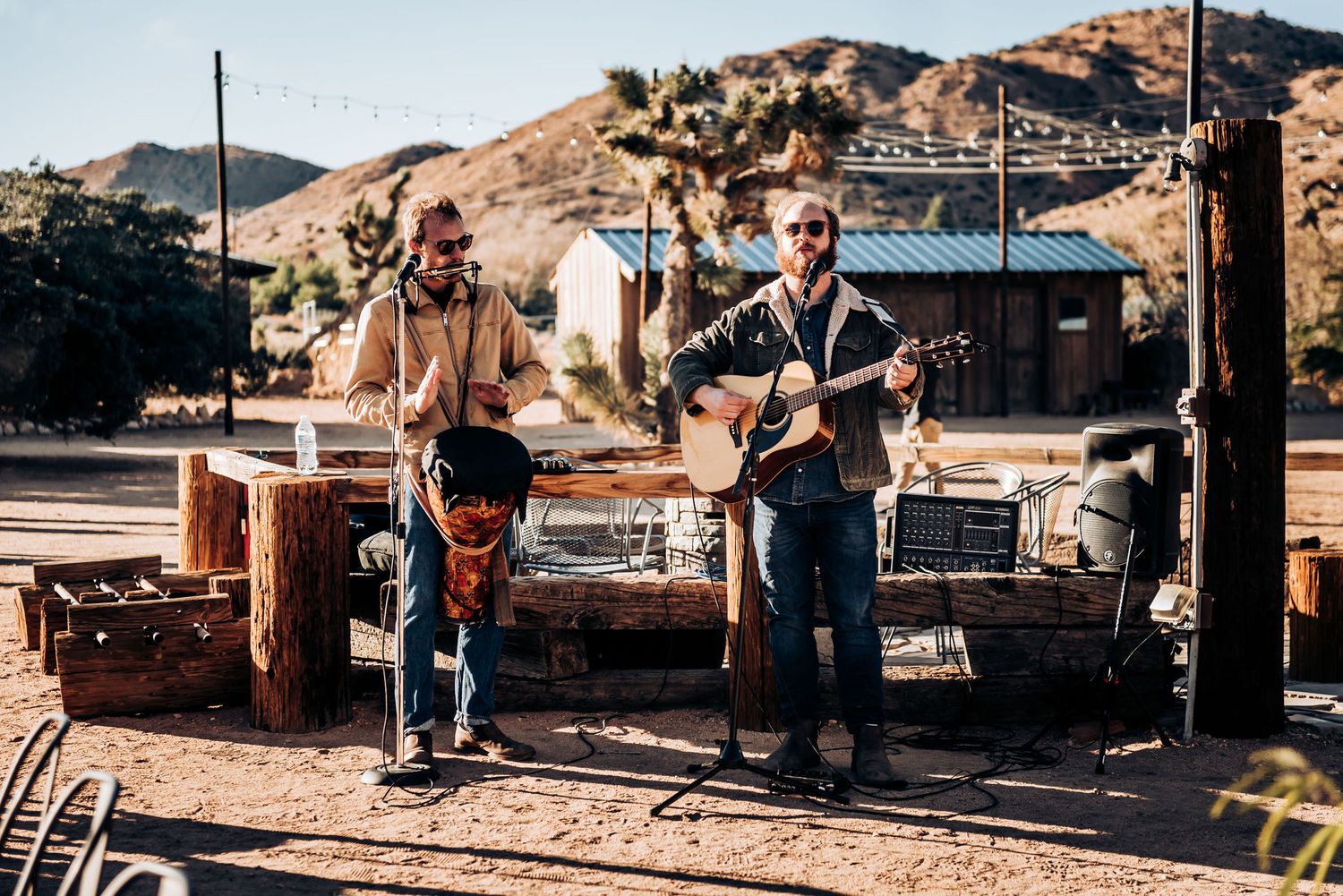 Musicians perform with acoustic instruments against a desert mountain backdrop.