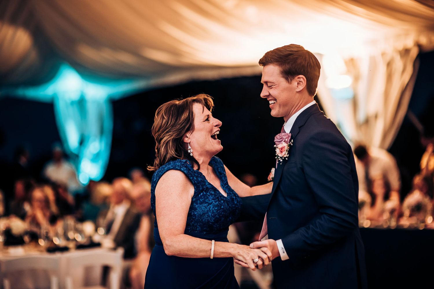 A lively dance moment captured during an evening wedding reception under draped fabric decor.