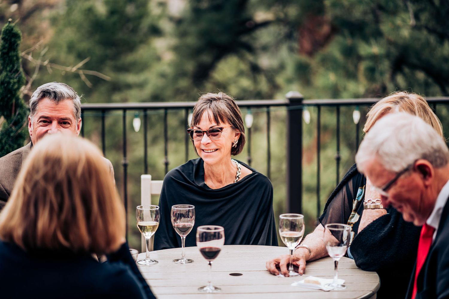 Wedding guests enjoy dinner and wine at an outdoor reception table.