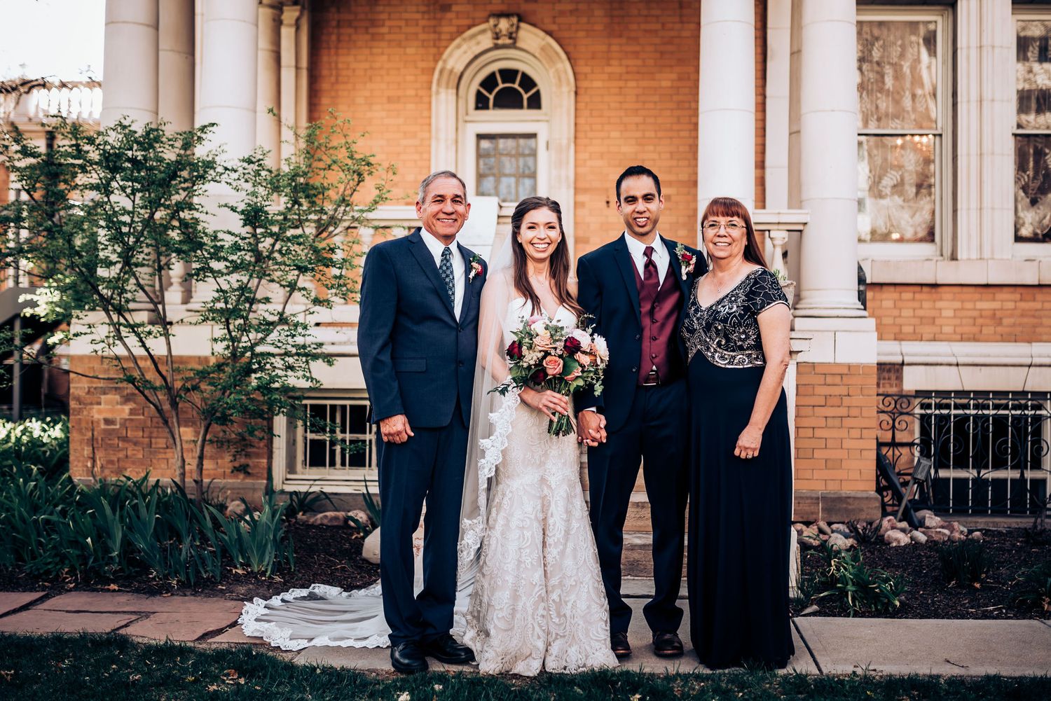 Wedding party poses for formal portrait outside historic brick building with white columns.