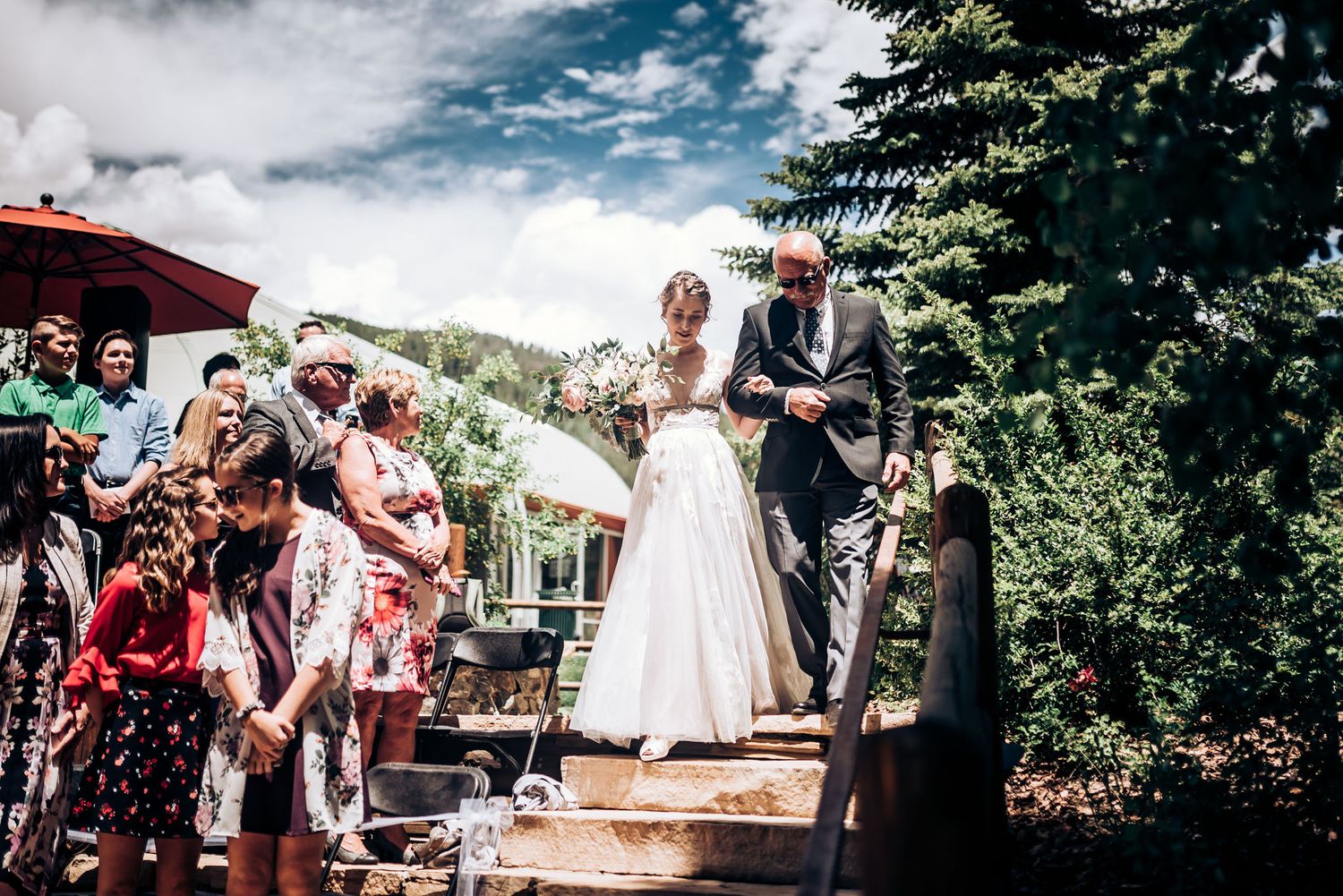 Outdoor summer wedding ceremony on wooden deck surrounded by pine trees.