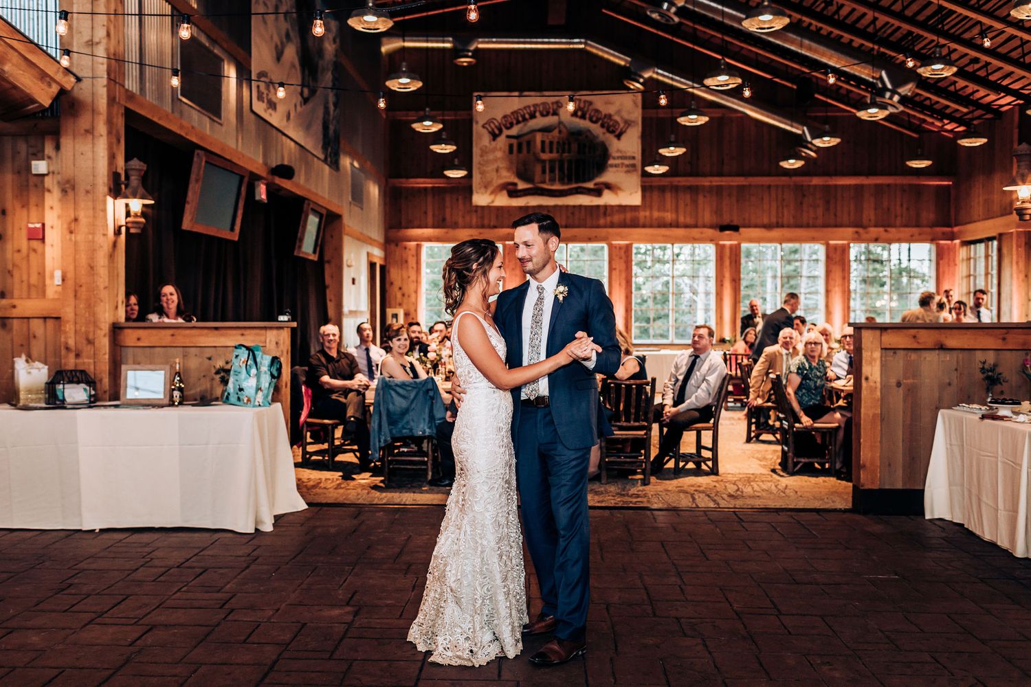 Wedding reception dance in rustic wooden venue with guests looking on.