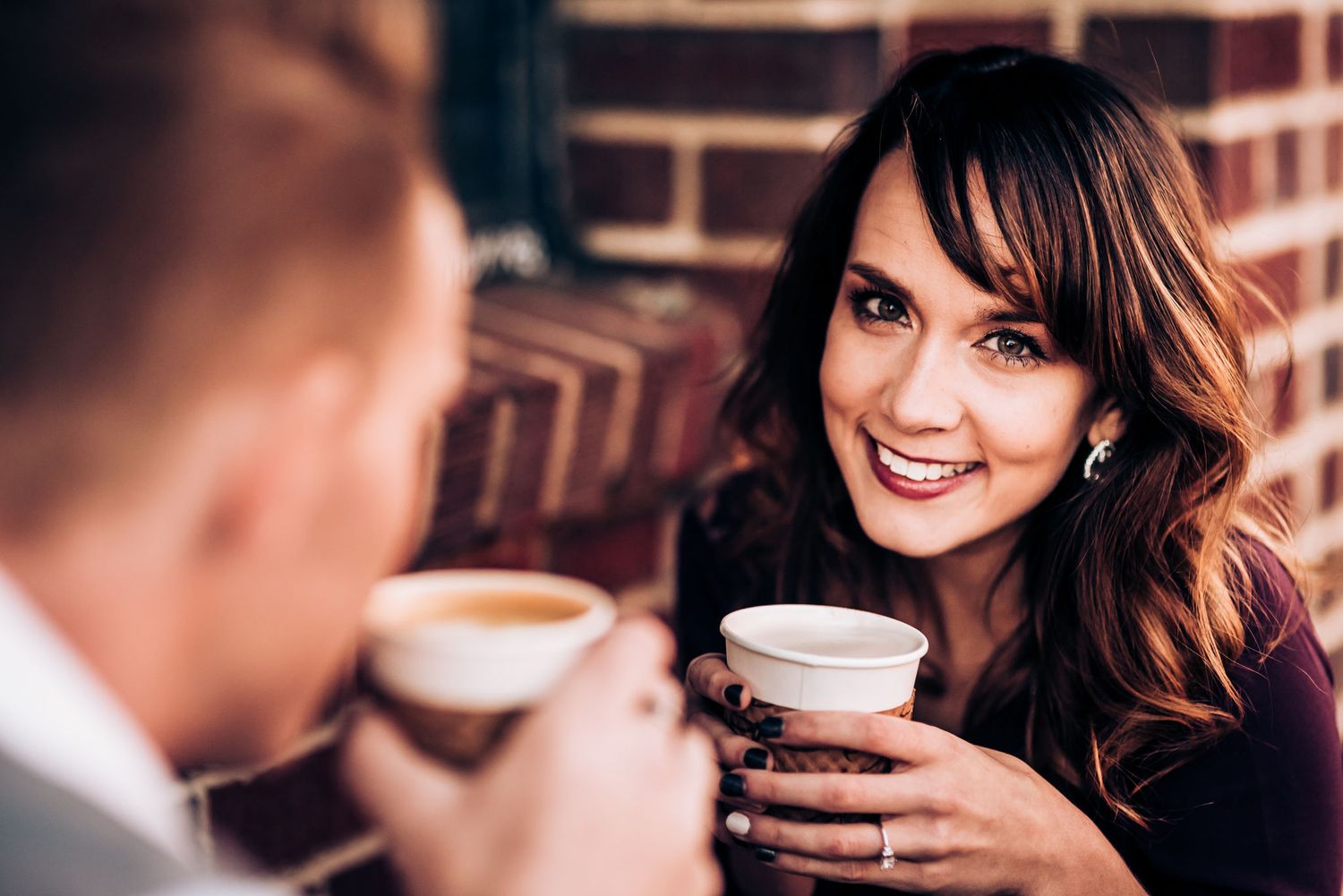 Couple sharing drinks and conversation at brick-walled cafe.