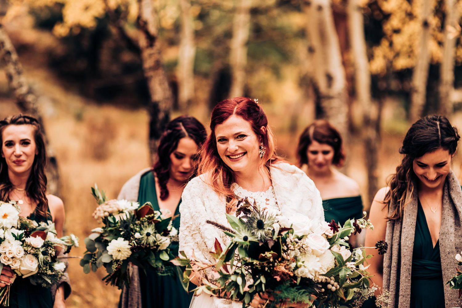 Bridal party walks together holding white and green bouquets against golden fall foliage.
