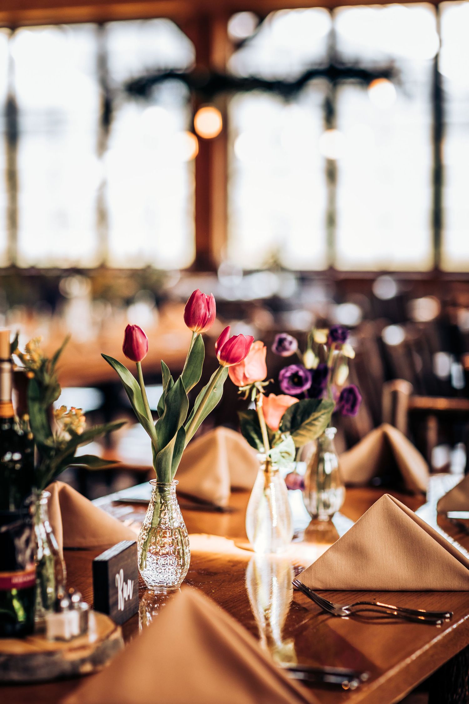 Table setting with red tulips in crystal vase and beige napkins at wedding reception.
