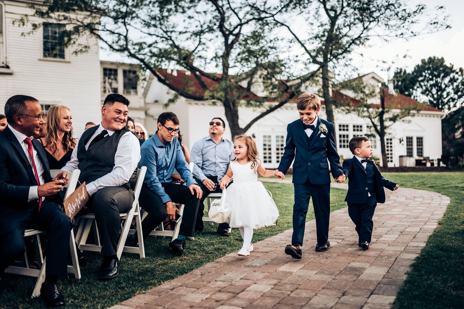 Wedding attendees seated on chairs along a brick pathway during an outdoor ceremony.