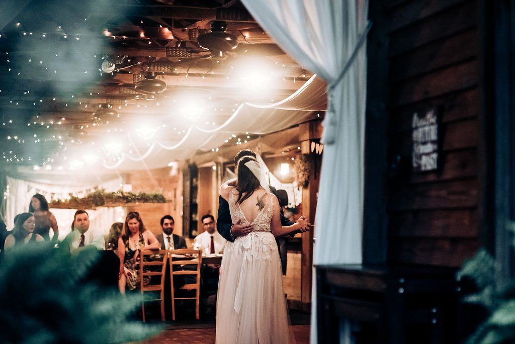 A dreamy wedding reception scene with fairy lights and white draping in a rustic venue.