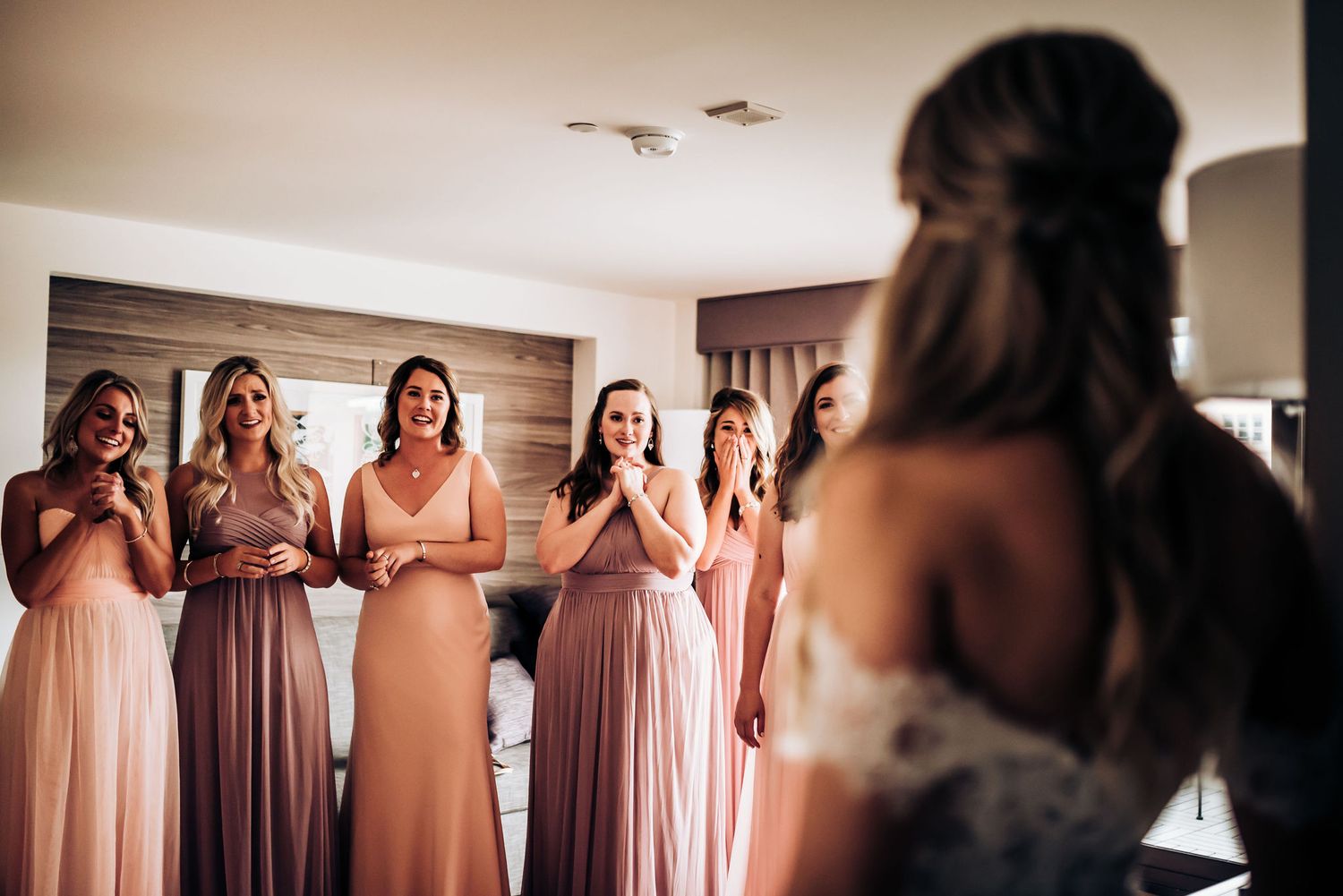 Bridesmaids in various shades of pink dresses share an emotional first look moment.