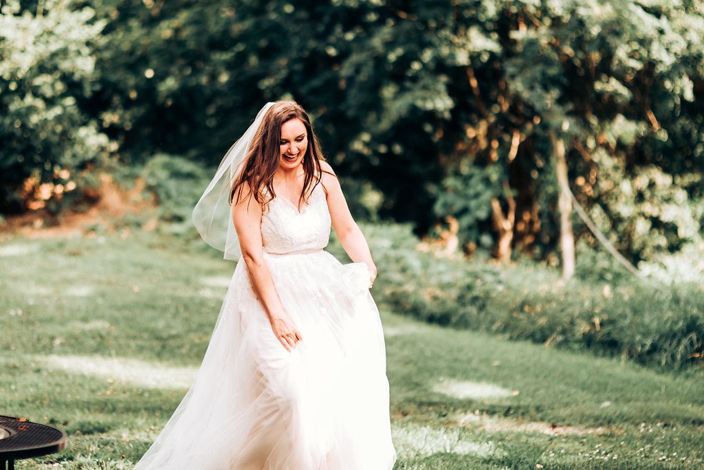 Bride in flowing white dress twirls joyfully in an outdoor garden setting.