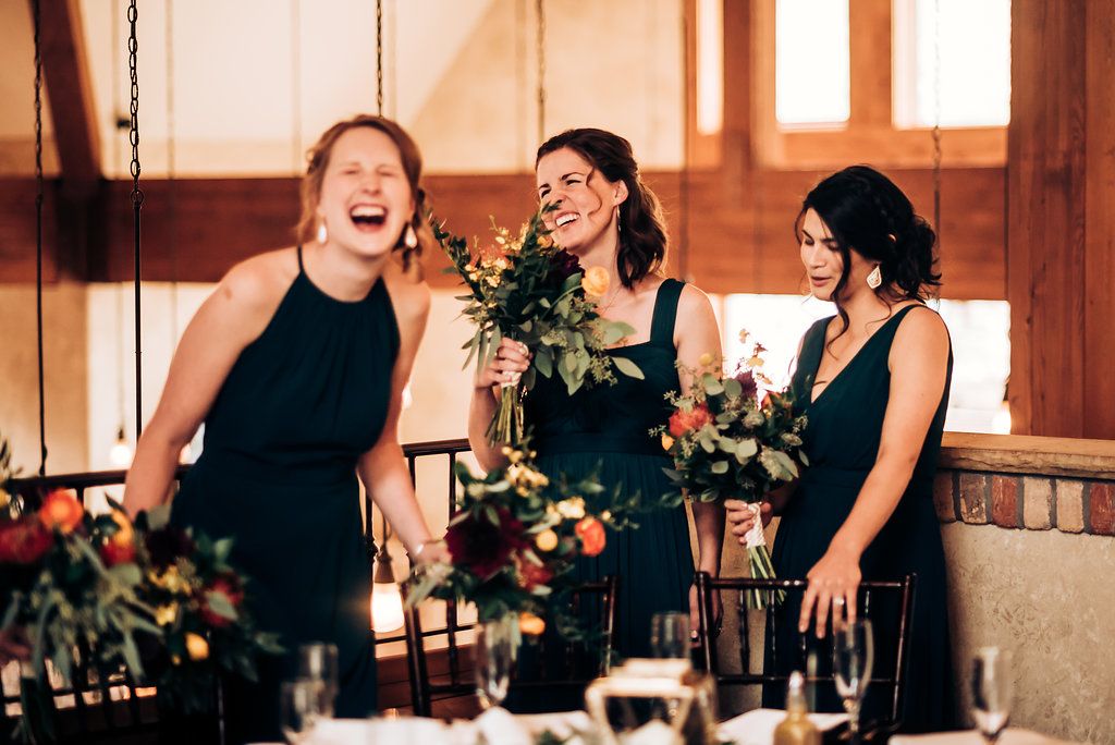 Three bridesmaids in navy dresses sharing a candid laughing moment at wedding reception.