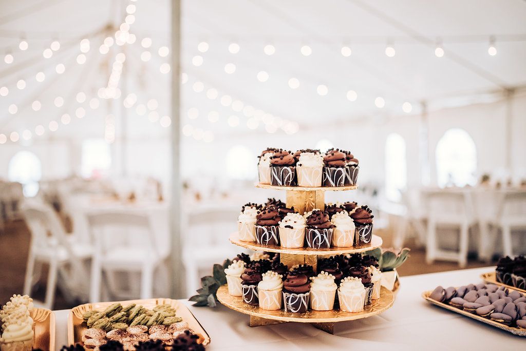 Tiered cupcake display with string lights and white tent backdrop at wedding reception.