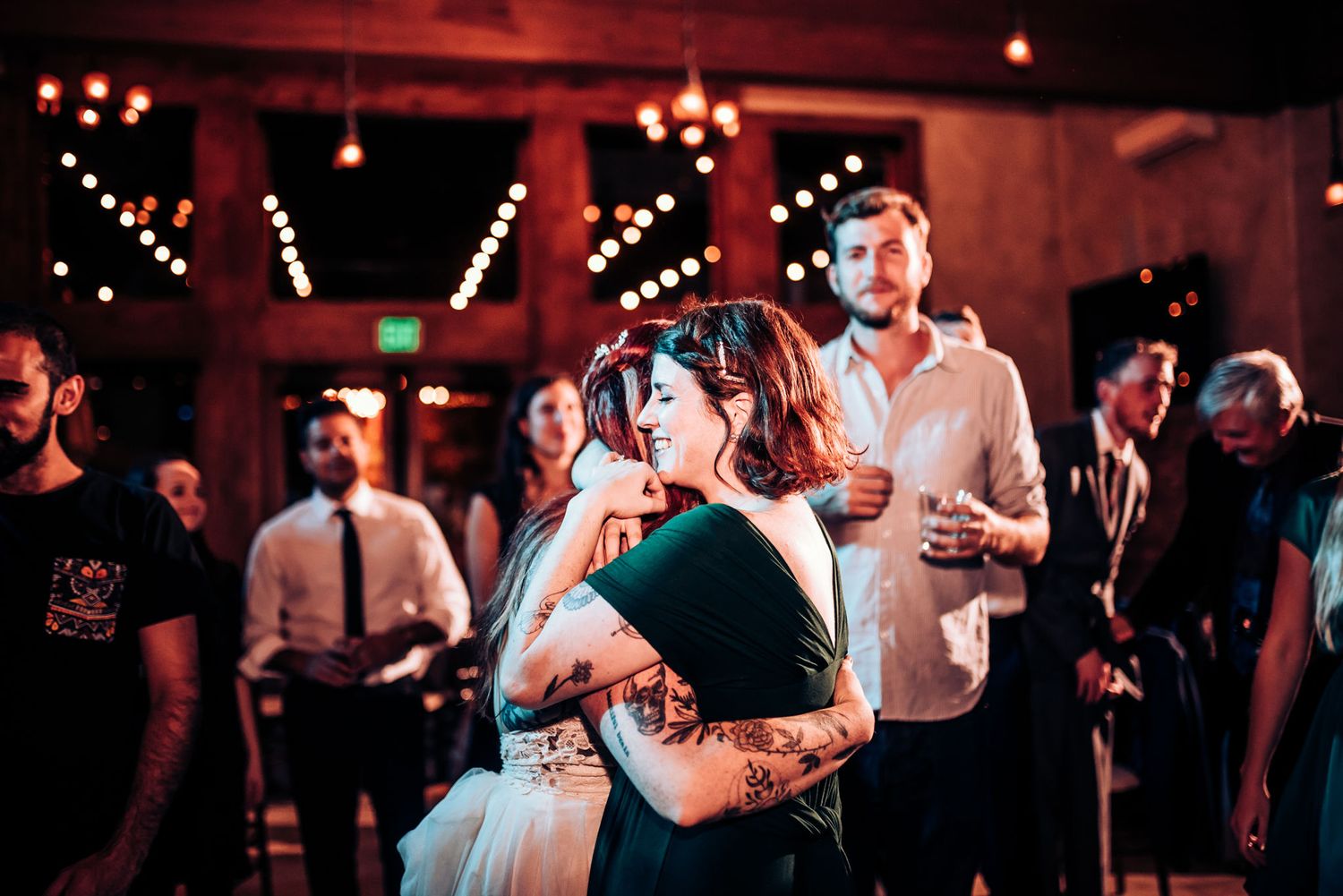 Couples slow dance under romantic string lights at an indoor wedding reception.