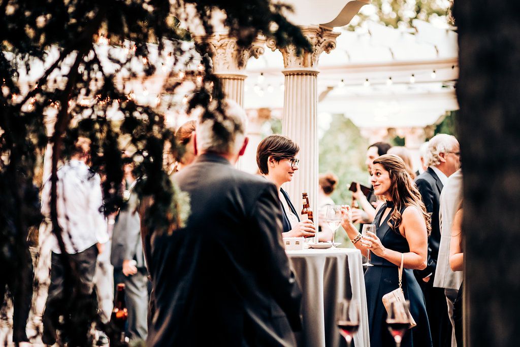 Guests mingle at an outdoor reception with string lights and columns visible in background.
