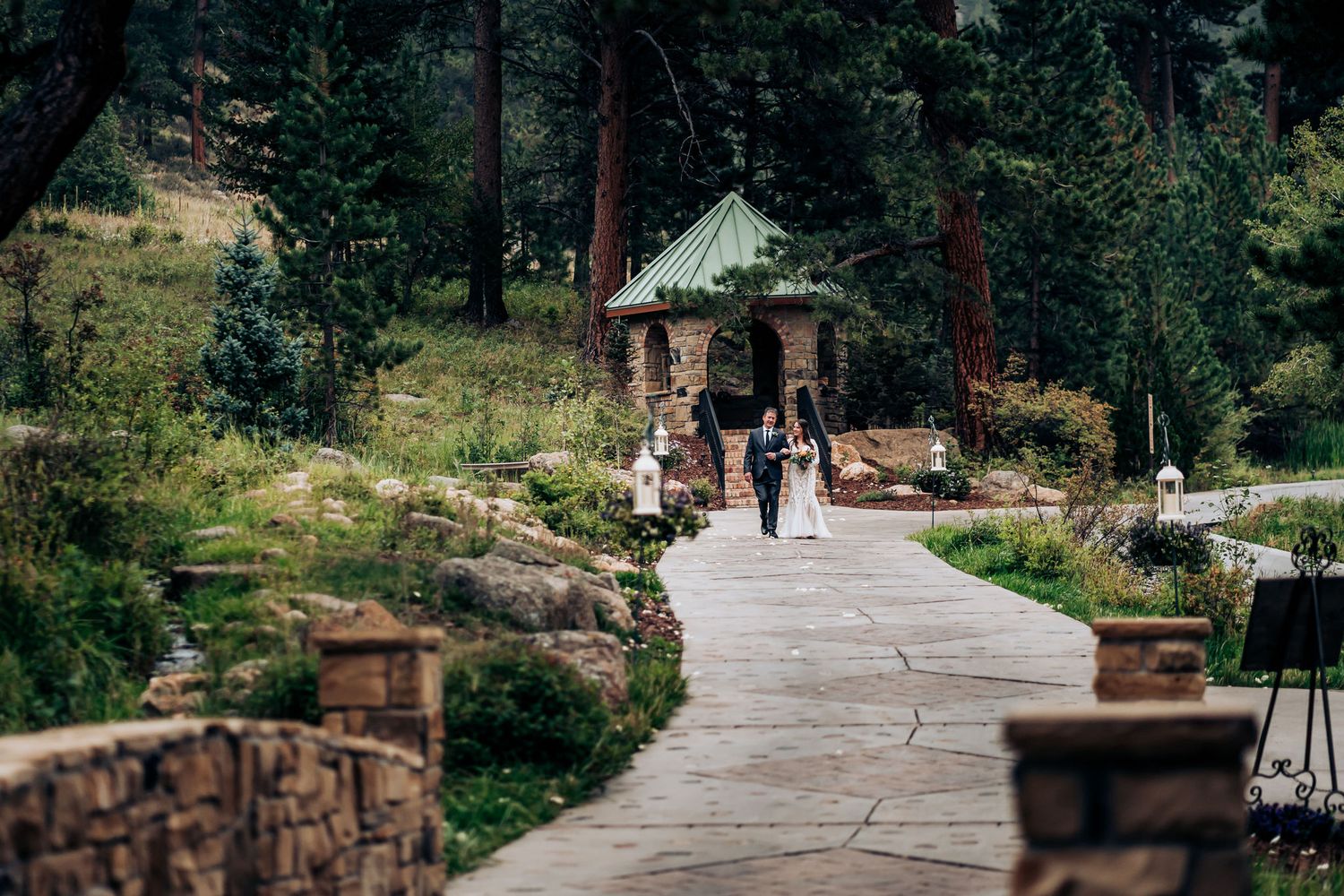 Stone-lined pathway leads to a gazebo surrounded by pine trees at a mountain wedding venue.