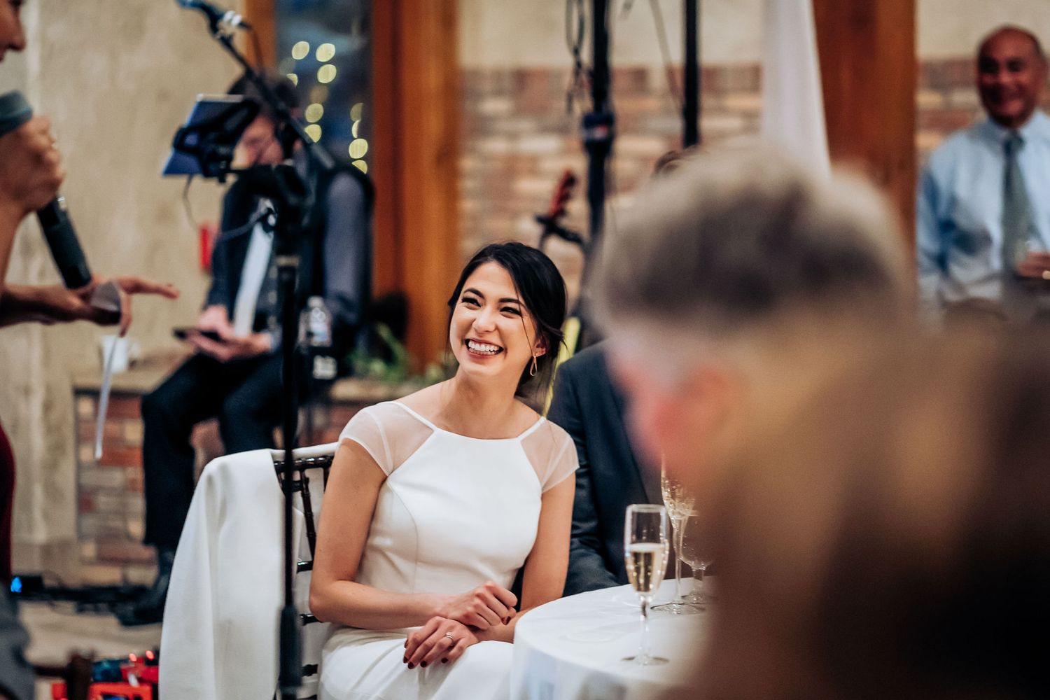 Joyful moment during wedding reception speeches with bride seated at table.