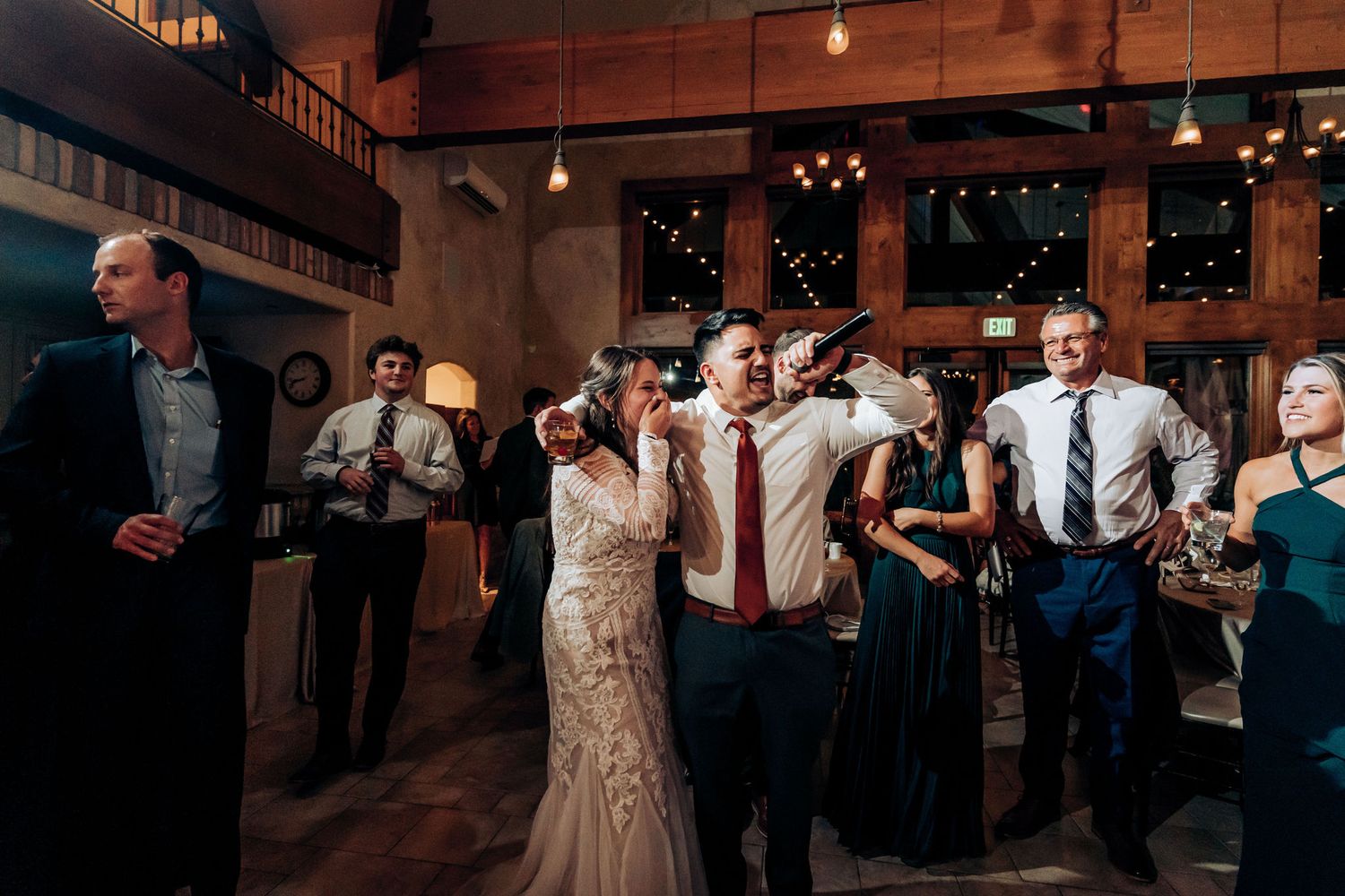 Wedding guests dance and celebrate in formal attire at rustic indoor reception venue.