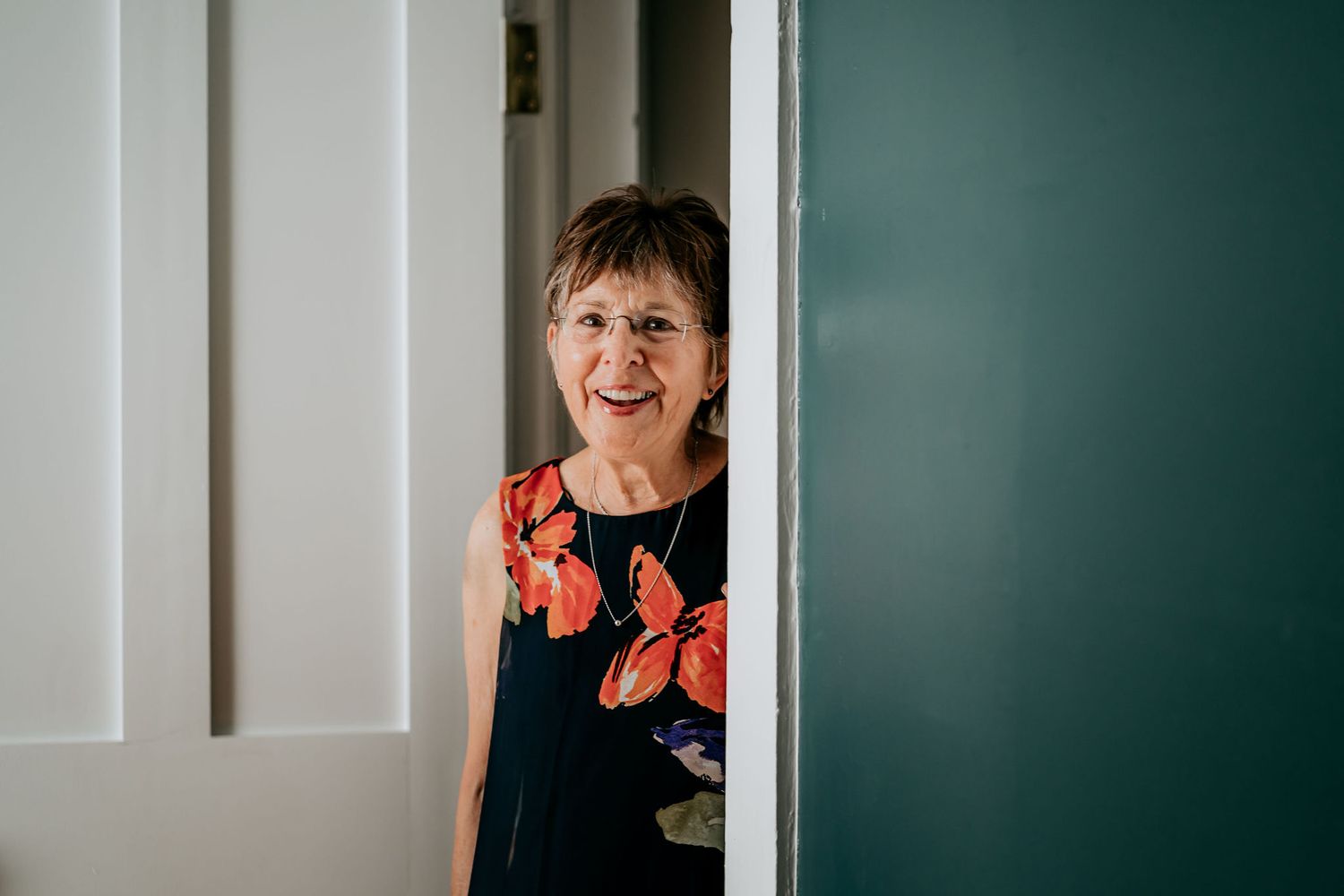 Someone peeks playfully around a doorway wearing a dark floral dress.