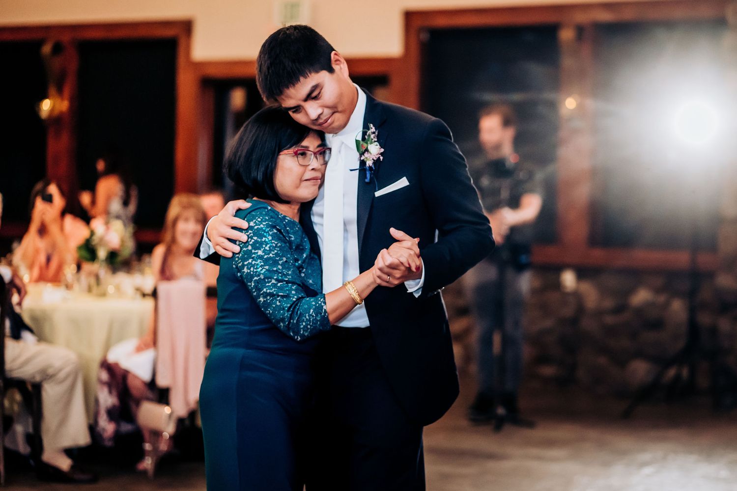 A couple shares an intimate slow dance at a formal wedding reception in elegant navy blue attire.