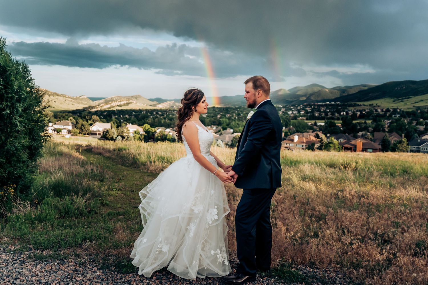 Dramatic wedding portrait with double rainbow and stormy skies over mountain landscape.