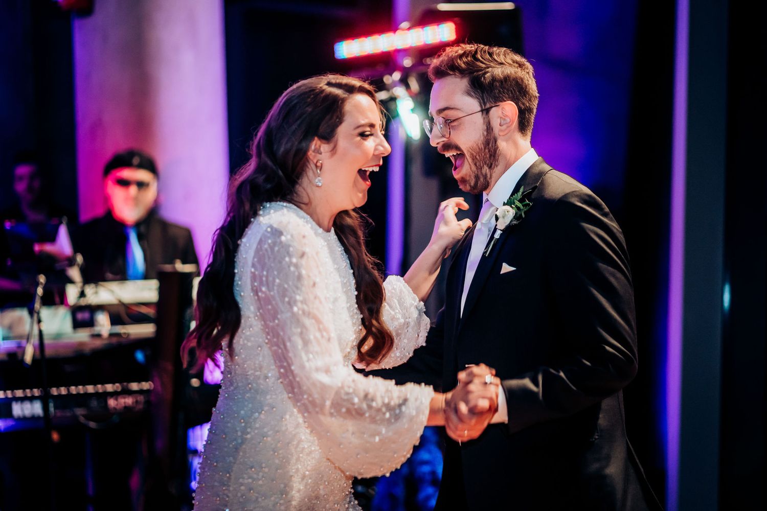 A couple laughs together while dancing at their wedding reception with band performing.