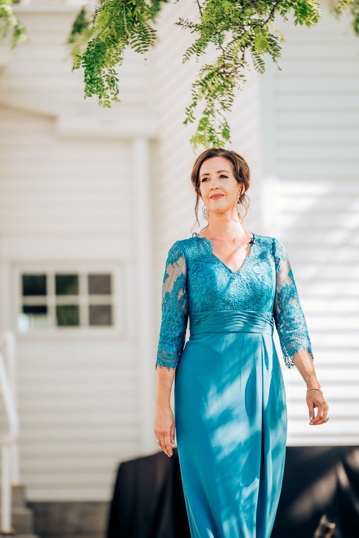 Woman in turquoise lace dress standing under greenery with soft lighting.