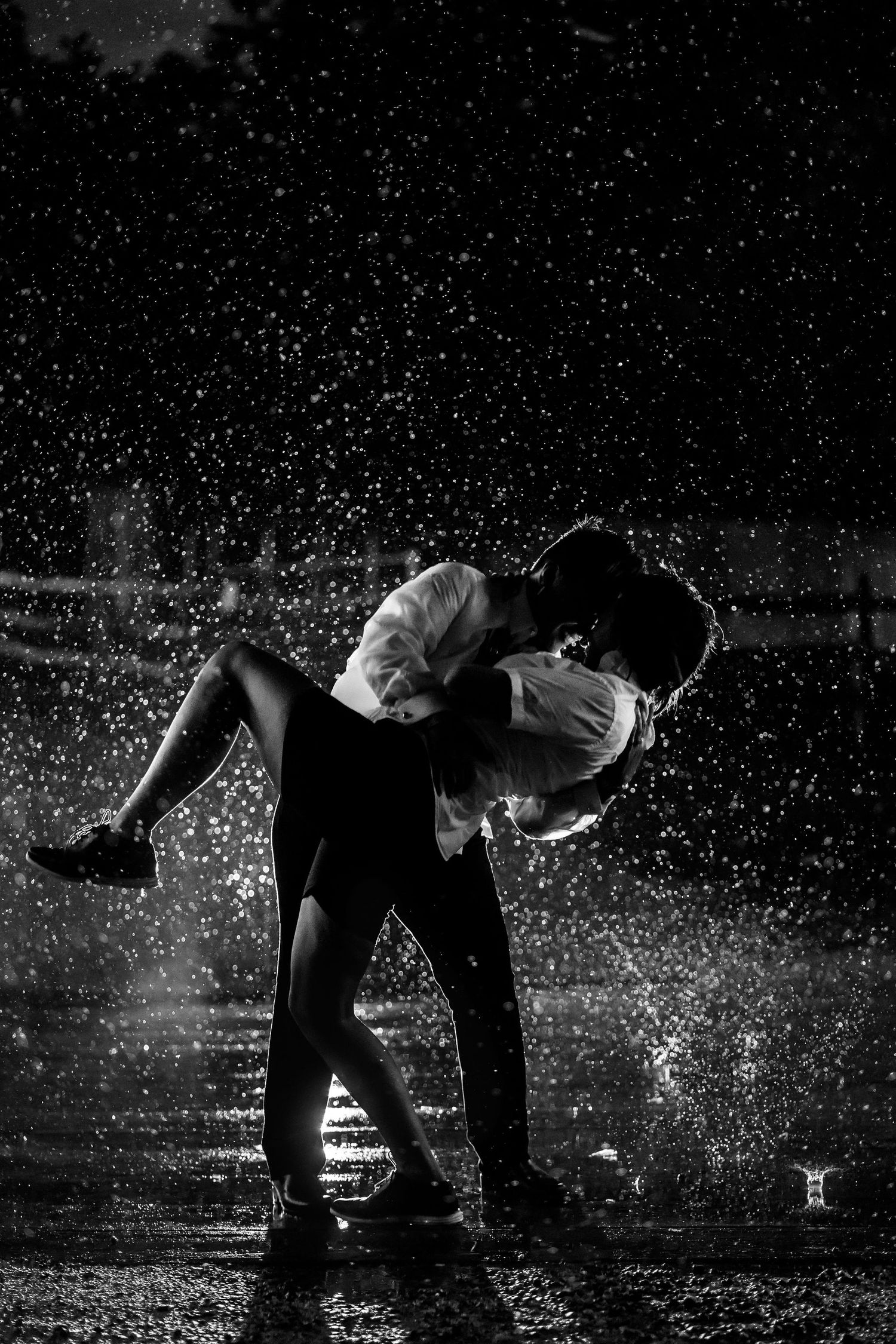 A dramatic black and white photo of a couple dancing in the rain.