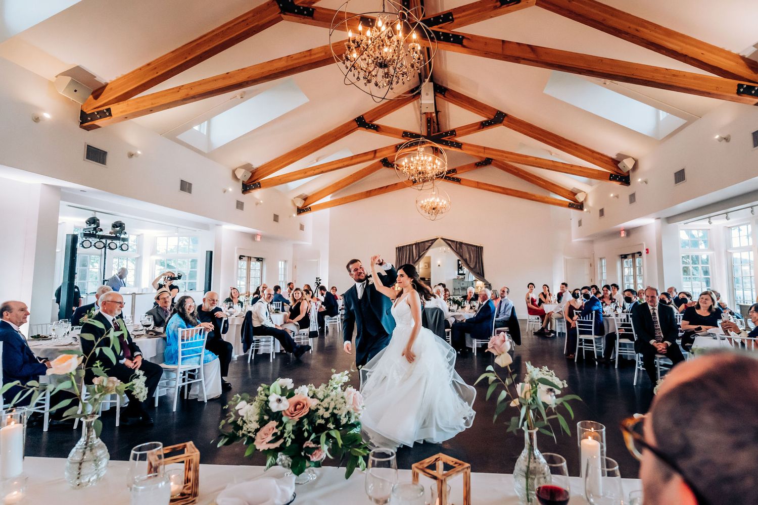 Wedding celebration in white chapel-style venue with wooden beam ceiling and elegant chandeliers.
