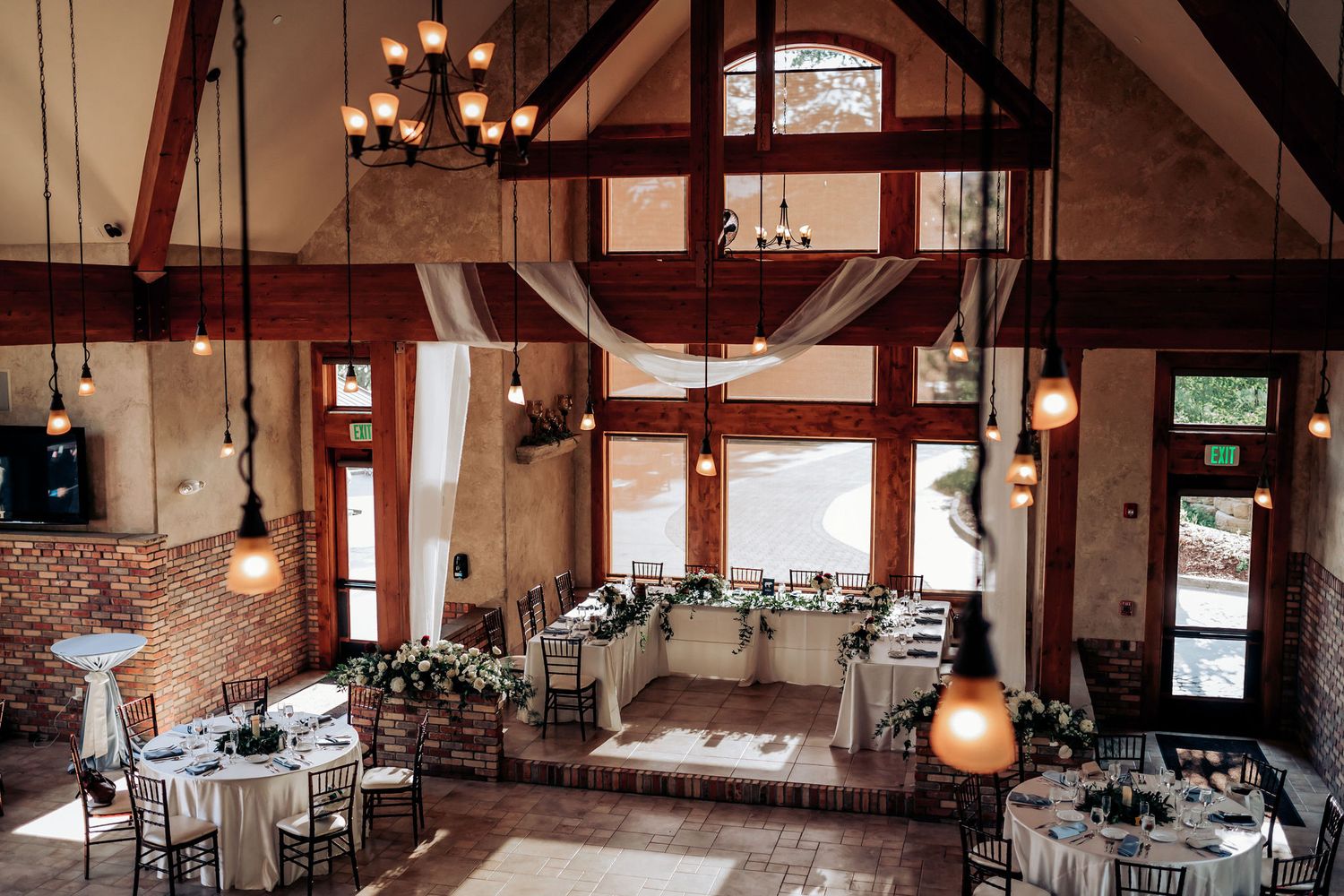 An elegant rustic wedding reception venue with exposed beams, chandeliers and draped fabric.