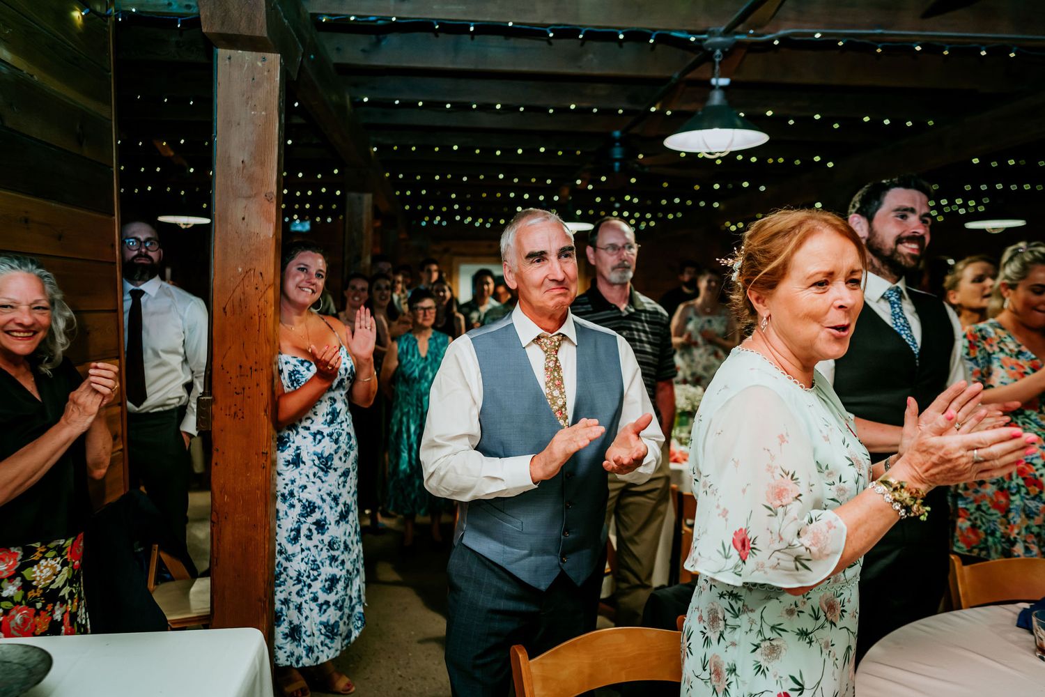 Wedding reception celebration with guests clapping and dancing under string lights.