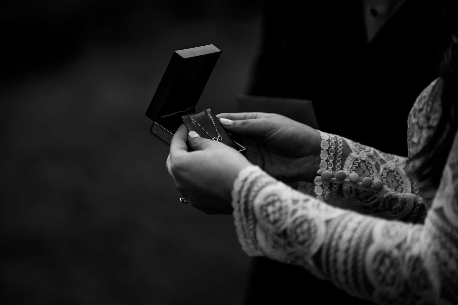 Close-up of lace-covered hands holding a small box in black and white.