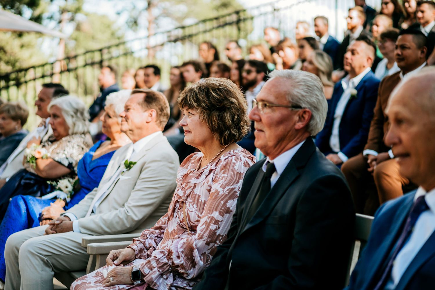 Wedding guests seated outdoors watching ceremony with emotional expressions.