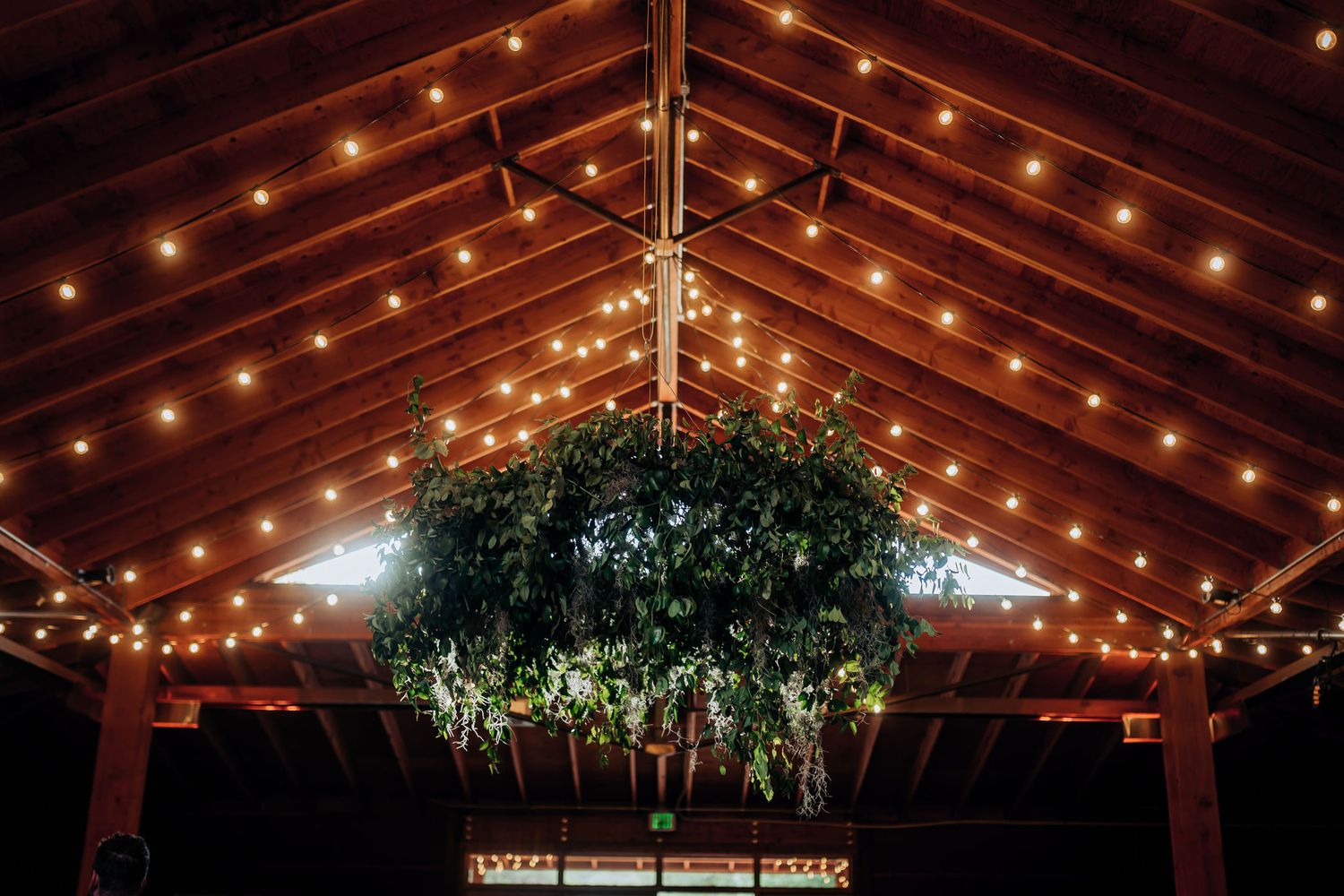 Rustic barn reception venue with wooden beams and hanging string lights creating warm ambiance.