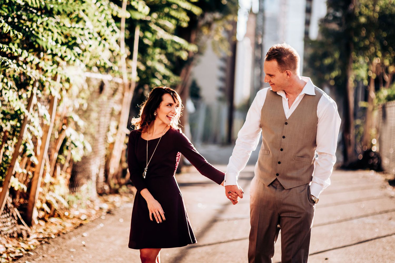 A couple holds hands while walking together on a tree-lined path.